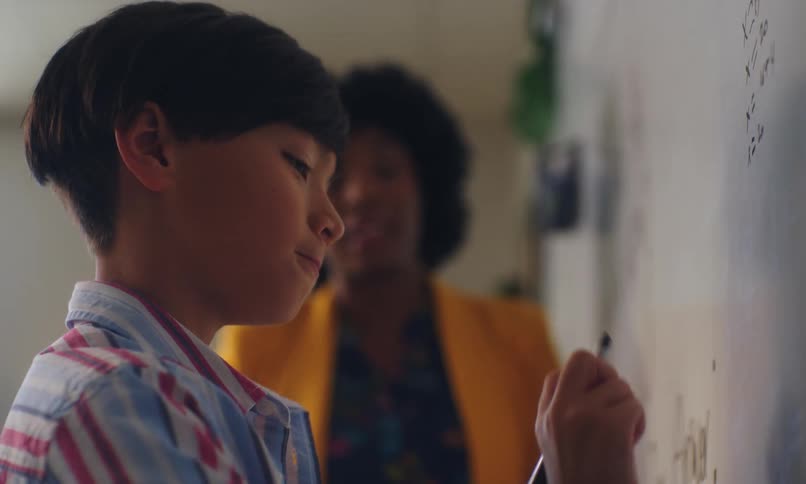 Boy writing on the whiteboard inside the classroom and touching hands with the teacher
