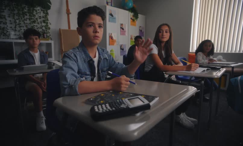 A student sitting in a classroom raises his hand to answer a question