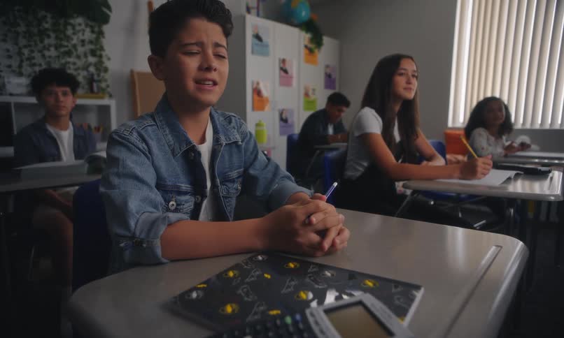 Students sitting at their desks in a classroom with one of them making a confused facial expression