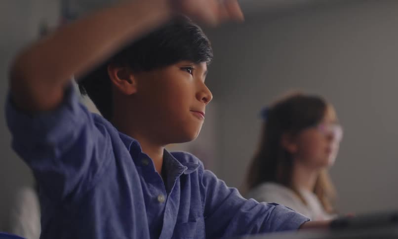 A young boy raises his hand attentively in class