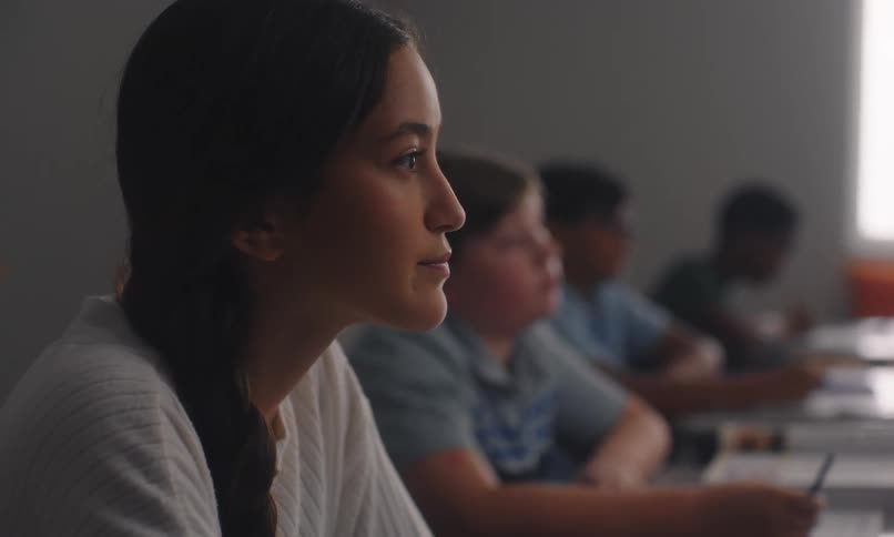 Students sitting in a row in a classroom with one of them raising his hands