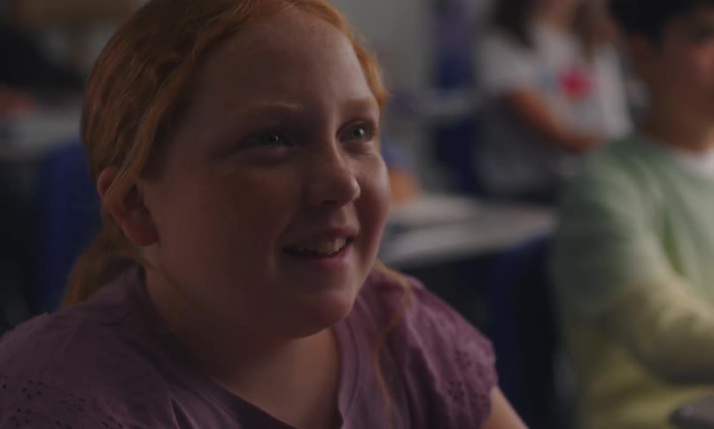 Portrait of a girl sitting in classroom with her hand raised talking
