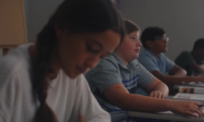 Students sitting at desktops on a classroom raise their hands to answer questions