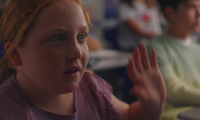 Redheaded female elementary school student sitting in class considers before raising her hand