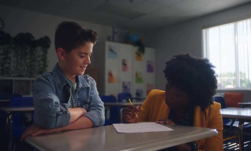 Teacher crouched down talking to a student inside a classroom