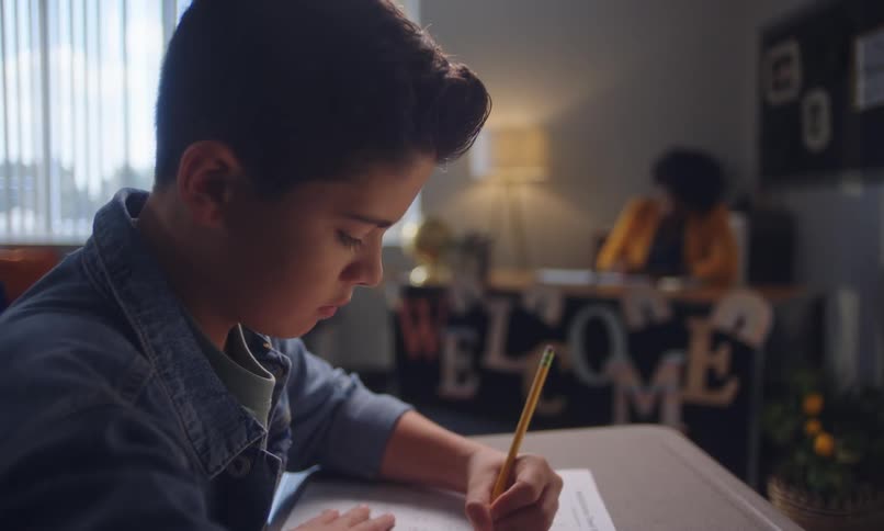 A young boy focused on writing at a desk in a classroom setting