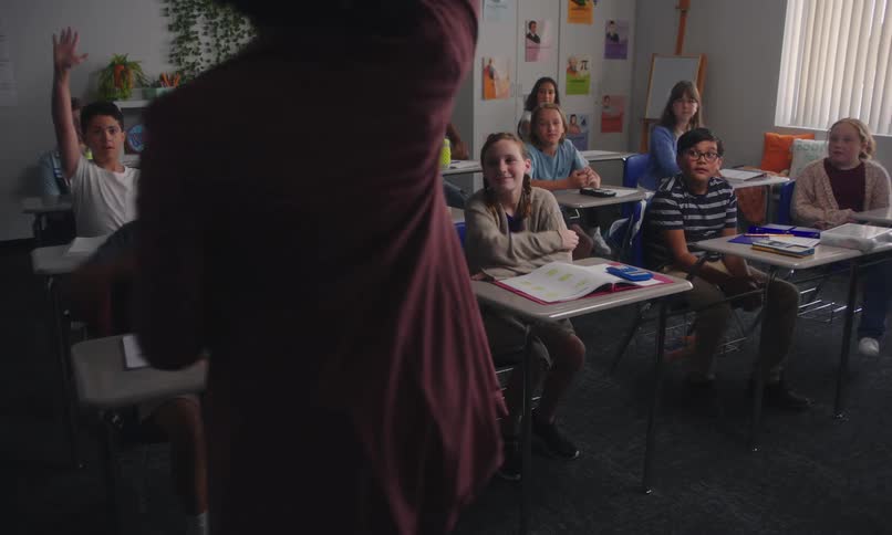 Teacher teaching in a classroom with several small students raising their hands