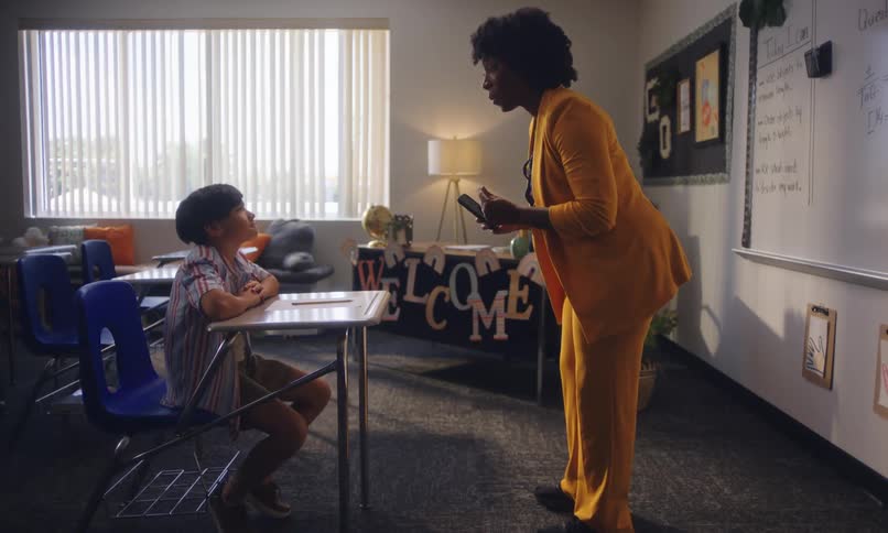 A teacher bends down to talk to a student in a classroom
