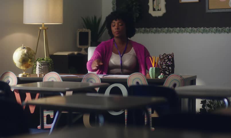 Female teacher sits at her desk in the classroom and starts writing