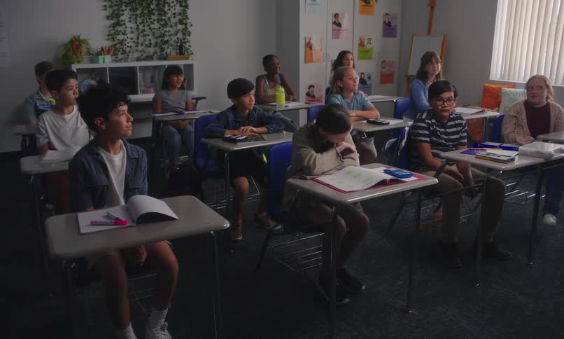 A classroom with students seated at desks facing a teacher standing at the front