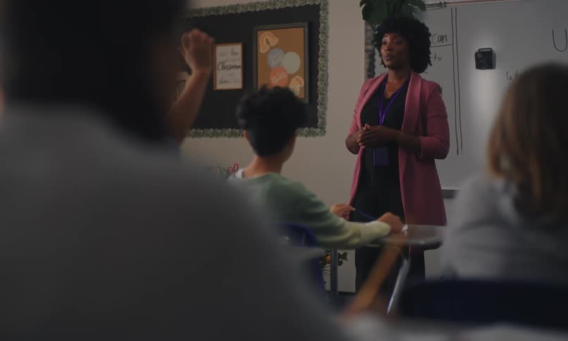 Teacher in a classroom talking to some students who raise their hands