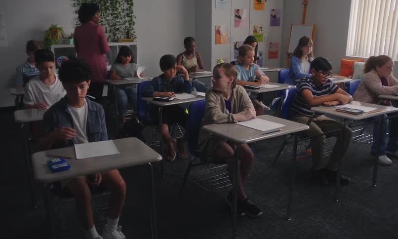 Teacher walking around passing out a test to her students in a classroom