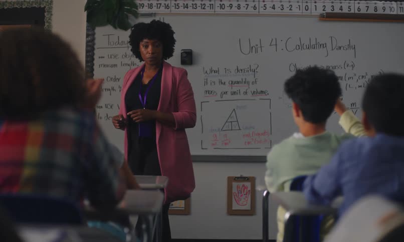 Teacher in a classroom teaching and students raising their hands