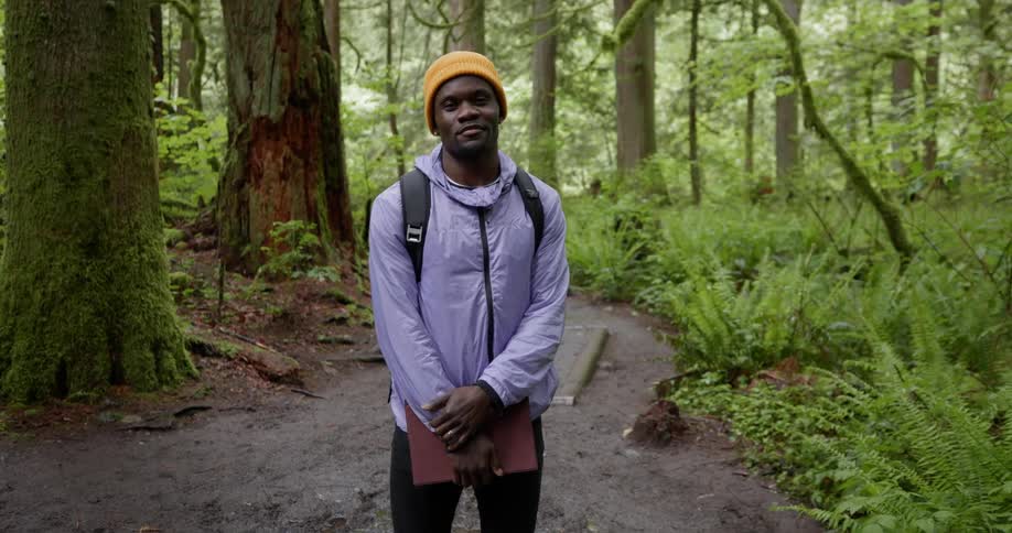 Man holding a laptop standing on a trail in a forest