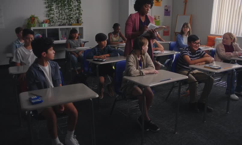 A teacher hands out papers to her students sitting in her classroom