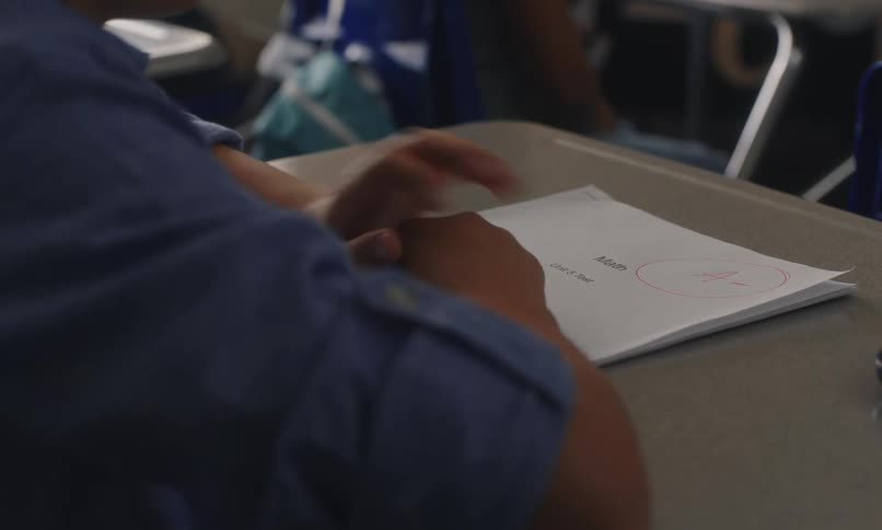 A child in a classroom focused on reading a his test results with other students visible in the background