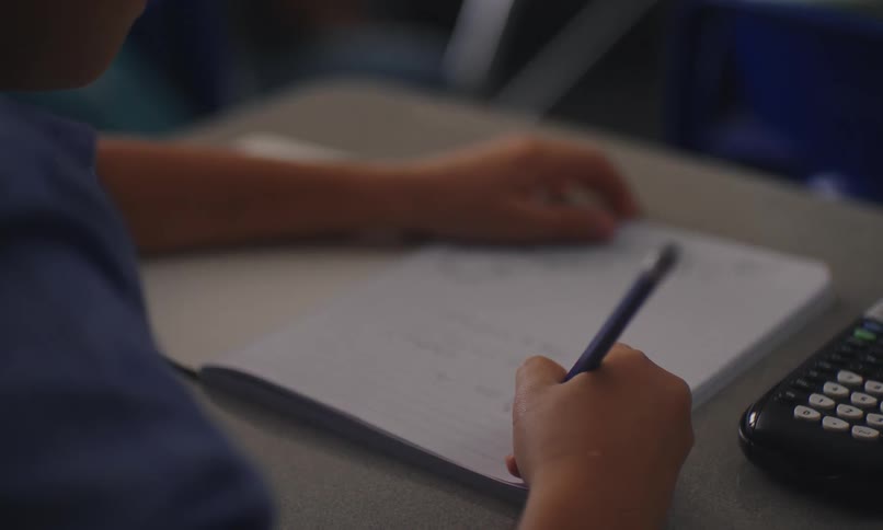 A young latino child writes in his notebook in a classroom