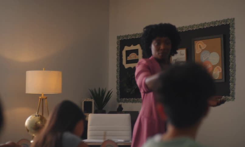 Teacher giving a class to students in the classroom with one of them writing in a notebook