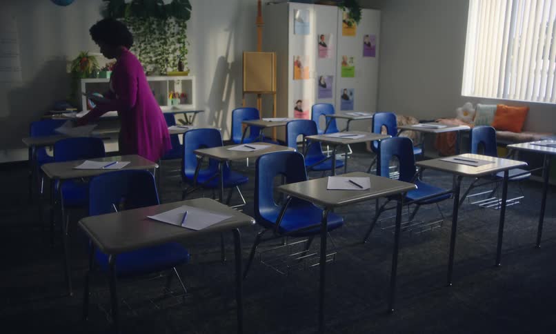 Teacher alone inside a classroom placing papers on students desks