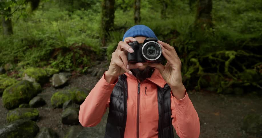 Female photographer putting professional camera to her face and while standing in a forest environment