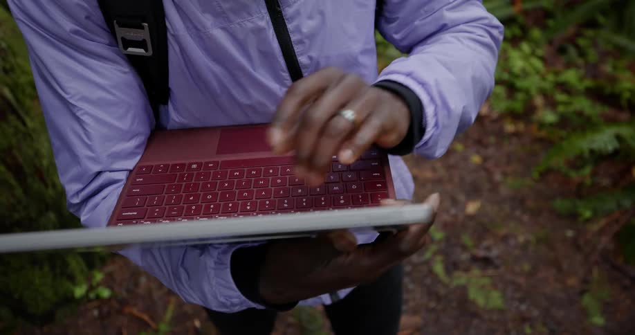 Person typing on laptop with red keyboard outdoors