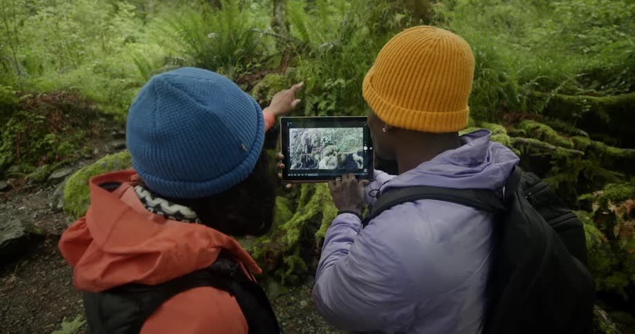 Two backpackers stand on trail and use a tablet to take pictures of the area