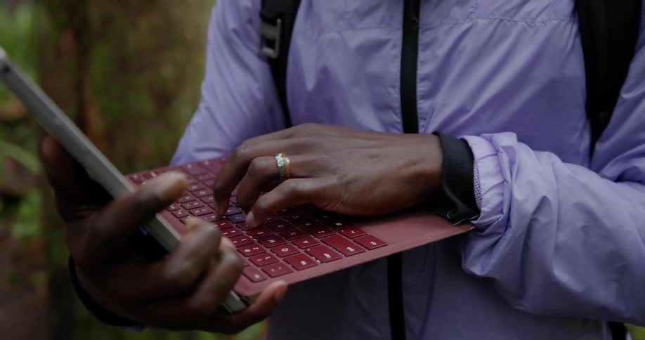 A man types on a laptop in the forest