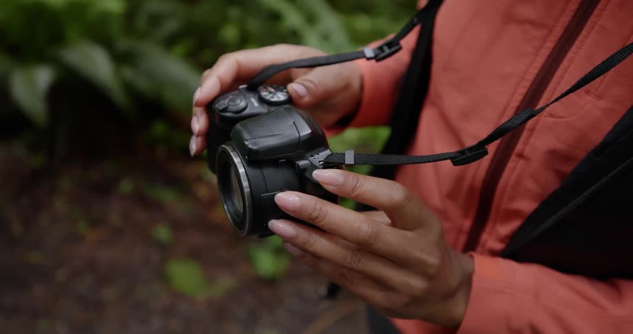 A woman adjusts her camera while standing in a forest