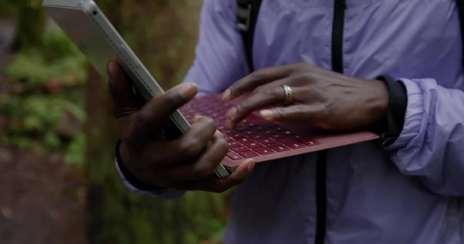 A persons wearing a purple jacket type on the keyboard of a red laptop