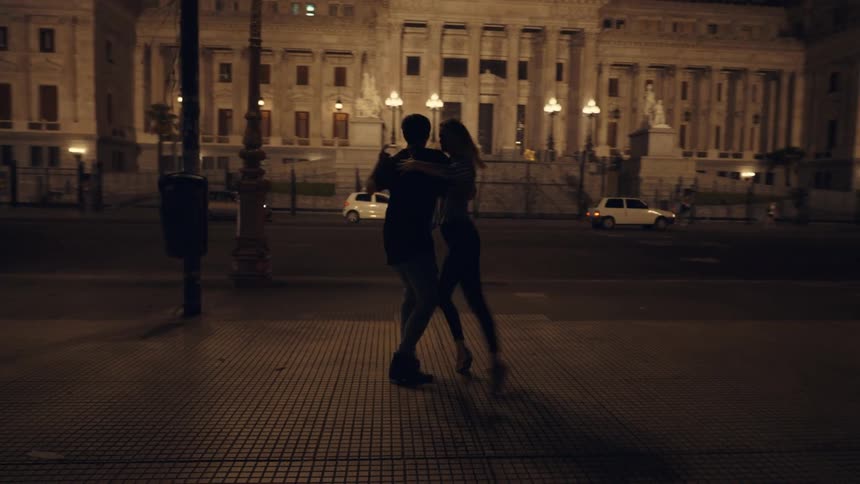 Silhouette of a couple dancing tango on the city streets at night