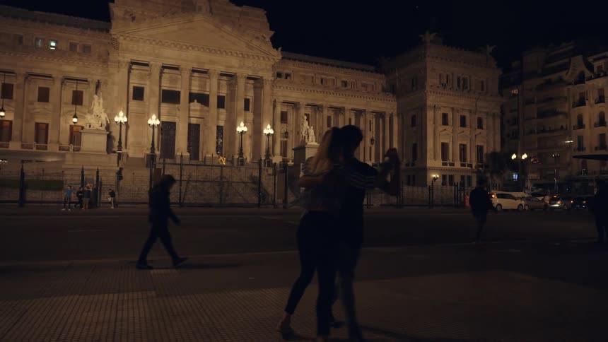 A couple dances in front of a grand illuminated building at night