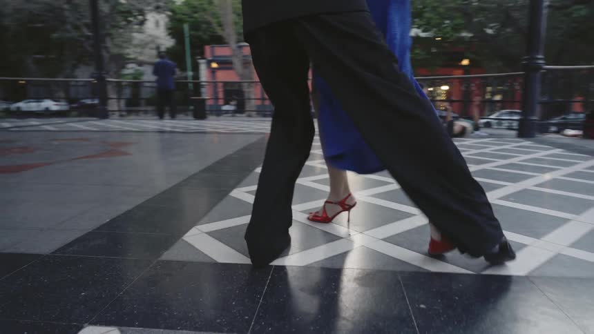 Close up of the legs of an elegant couple dancing on a black and white checkered floor in the city
