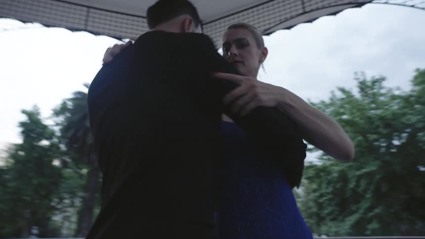 Man in suit and woman in blue dress dancing tango together in an outdoor space