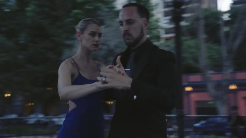 A man and woman dance in public as the camera pans around them