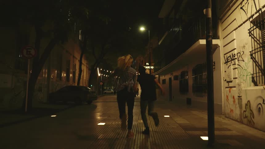Man and woman holding hands and running in an alley at night with low lighting