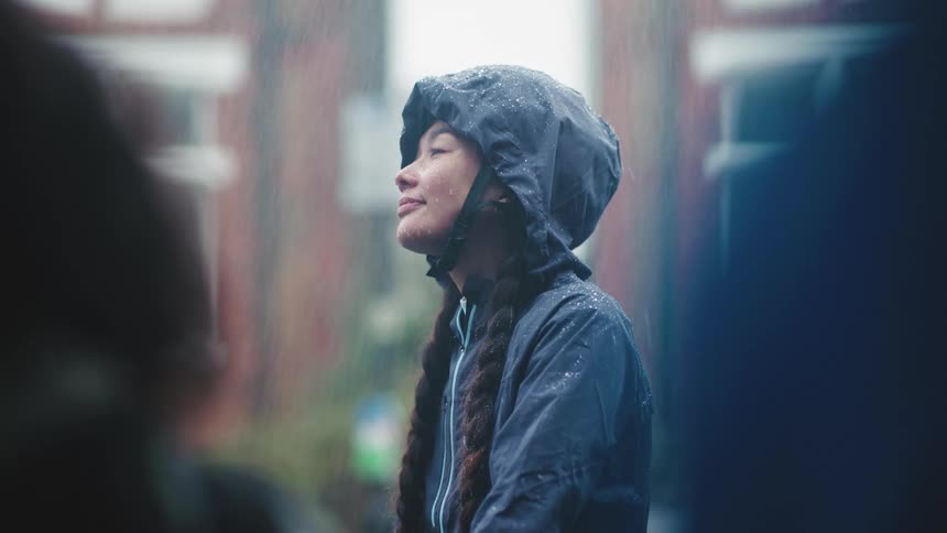 A woman with braided hair wearing a hooded jacket standing in the rain
