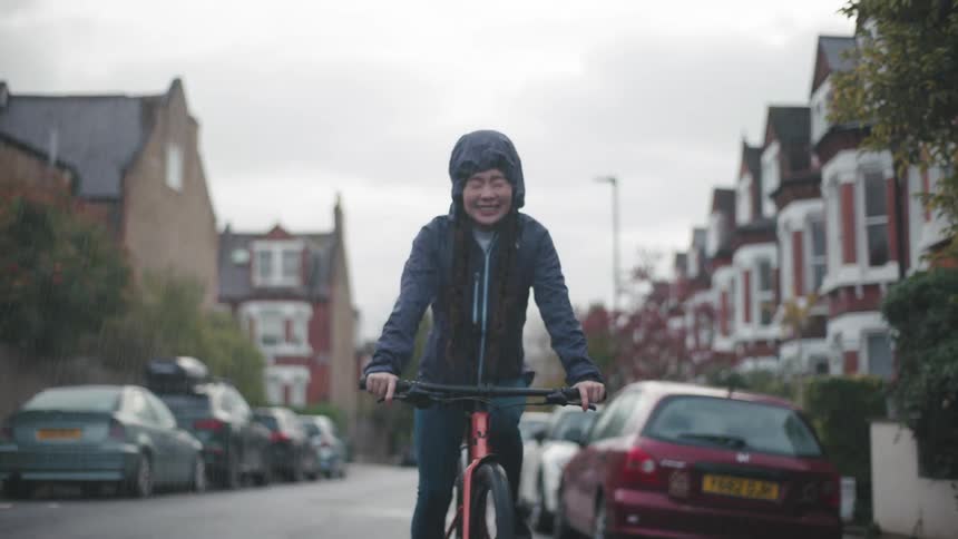 Woman smiles while riding her bicycle along a residential street in the rain