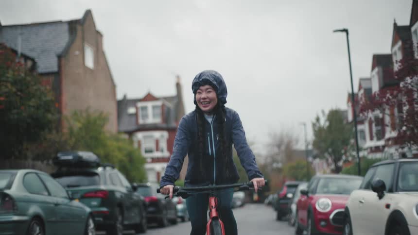 A young asian woman bicycles in a suburb on a rainy autumn day