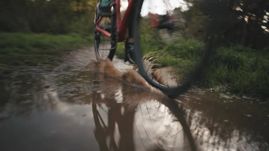 Person cycling in a rural environment passing over a puddle of water with mud