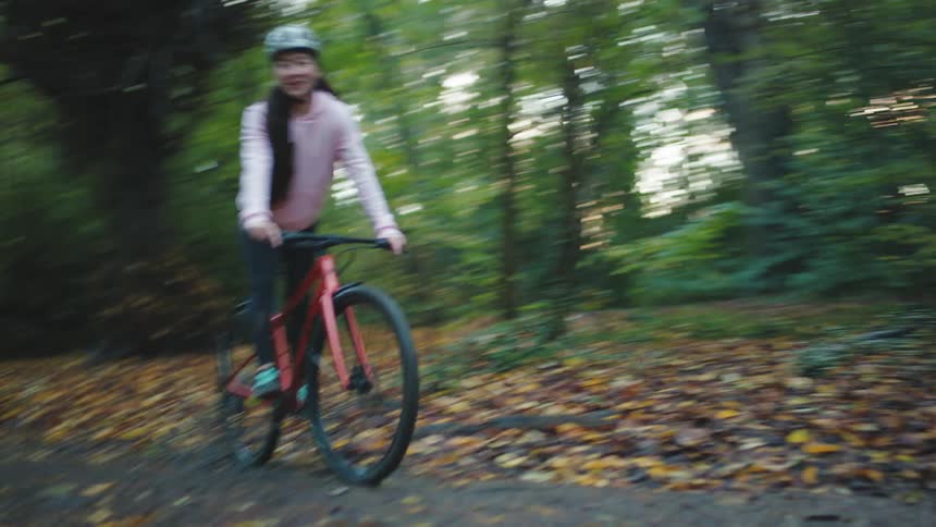 Woman riding a bike along a trail in a forest with trees around