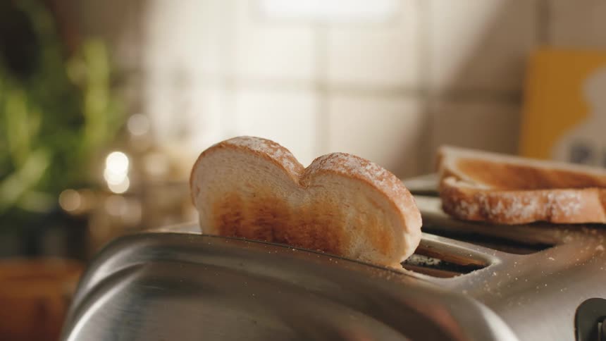 Two slices of bread perfectly toasted pop out of a stainless steel toaster