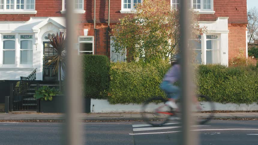 A cyclist riding a bicycle on a street viewed through vertical bars with residential buildings in the background