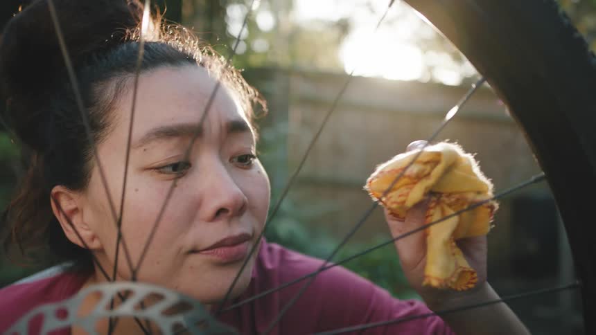 Woman cleaning the spokes from her bicycle tire with a yellow rag