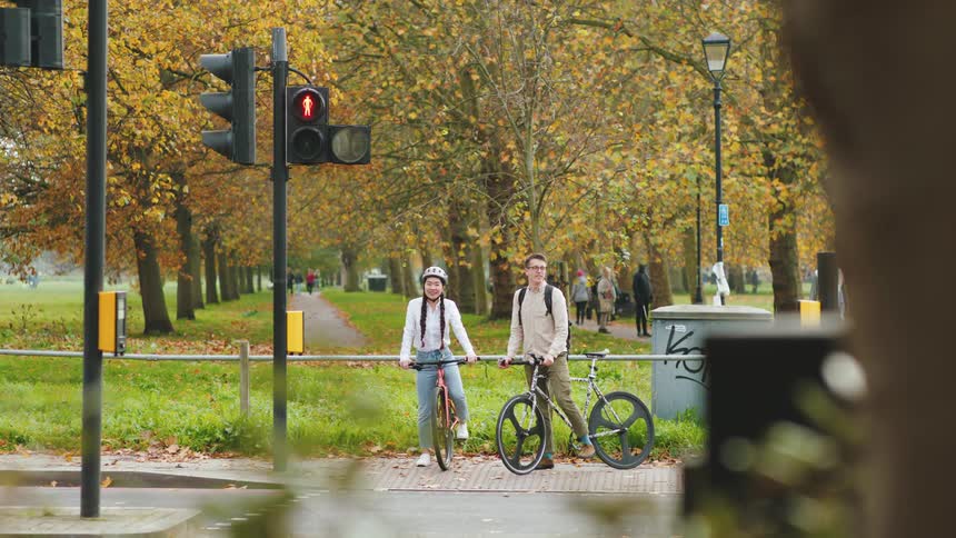 Two friends with bicycles stand at a crosswalk waiting for the red traffic light