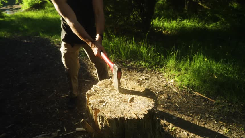 Man splitting a wood with an axe on a wood stump outdoors