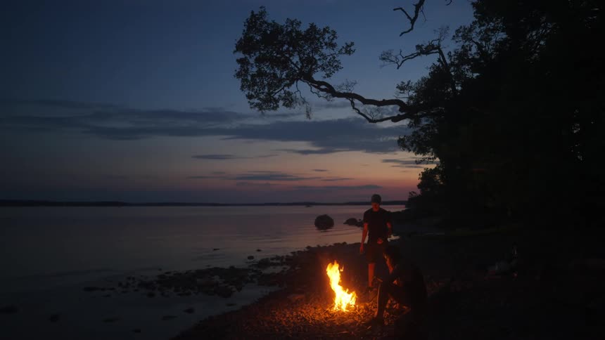 A person standing by a bonfire on a beach during twilight