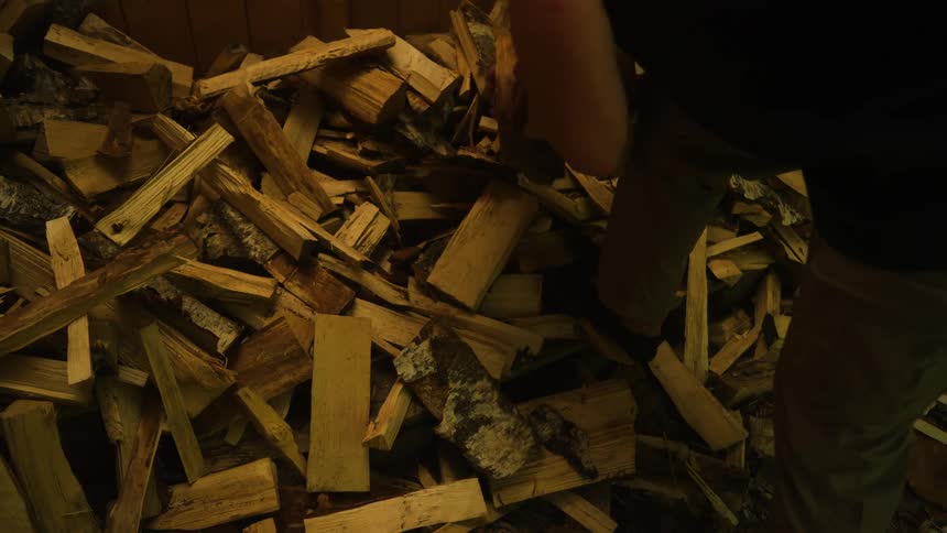 A large pile of chopped firewood with a person picking up some pieces