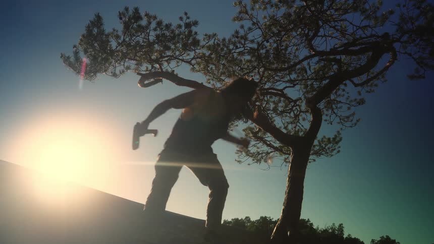 A silhouette of two people using a rope tied to a small tree to climb down a small slope