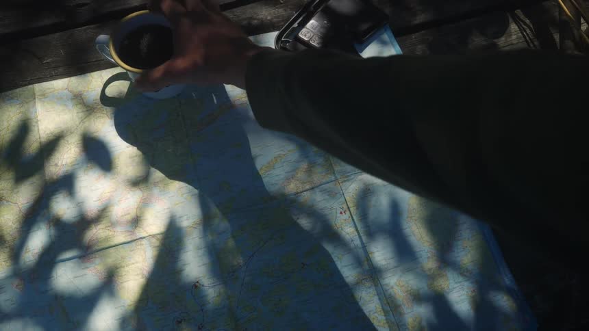 A hand reaching for a cup of coffee over a cartographical map under tree shadows