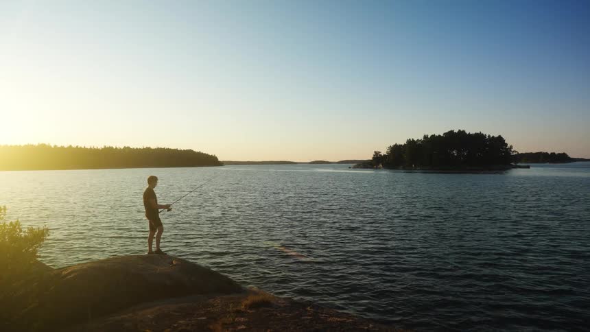 Man standing on a rock casting a fishing in the lake